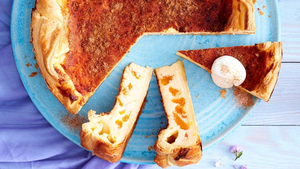 Drei Stücke vom Blätterteig-Schmand-Kuchen mit dem restlichen Kuchen auf einem blauen Teller vor blauem Hintergrund.