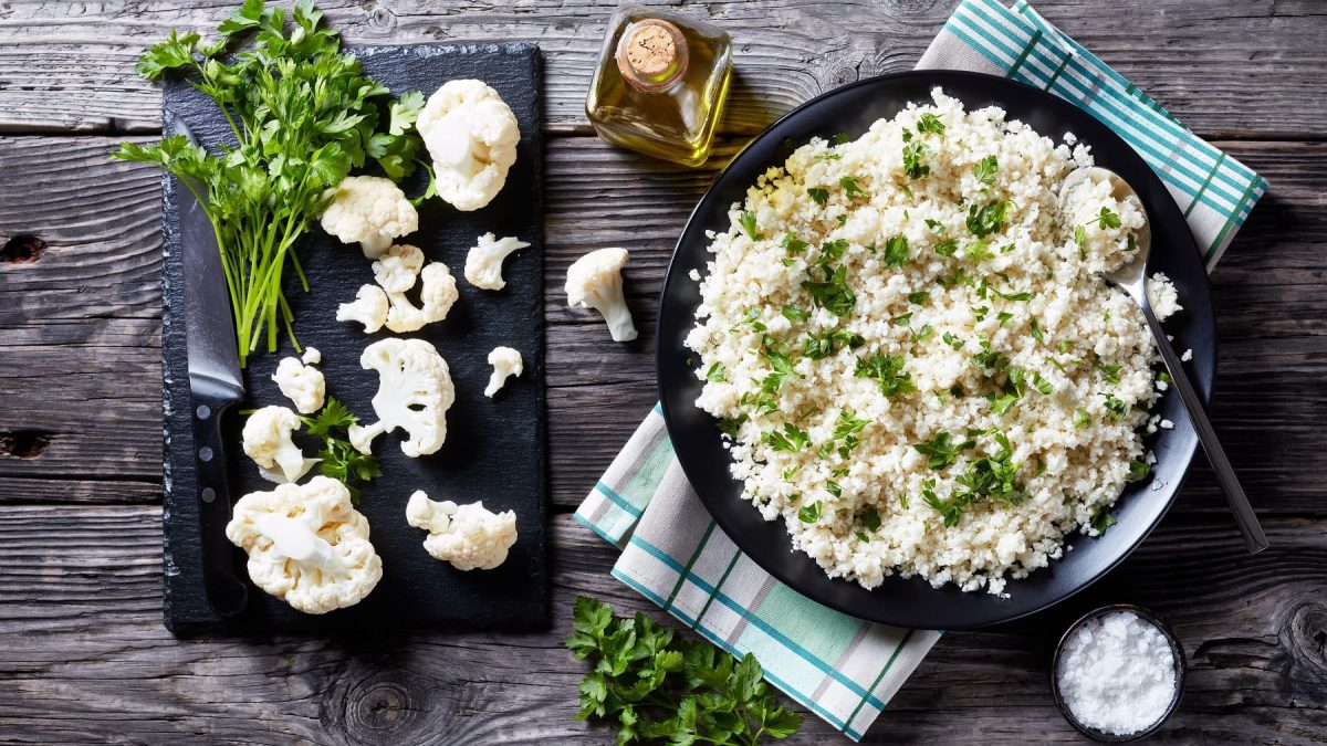Ein Teller Blumenkohl-Reissalat mit Petersilie bestreut in der Draufsicht, daneben Limettenspalten.