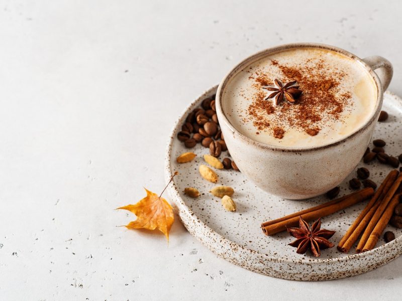Eine Tasse Chai Vanilla Coffee mit Anis und Muskat dekoriert, auf der Untertasse lieben Gewürze wie Zimtstangen und Kardamom.