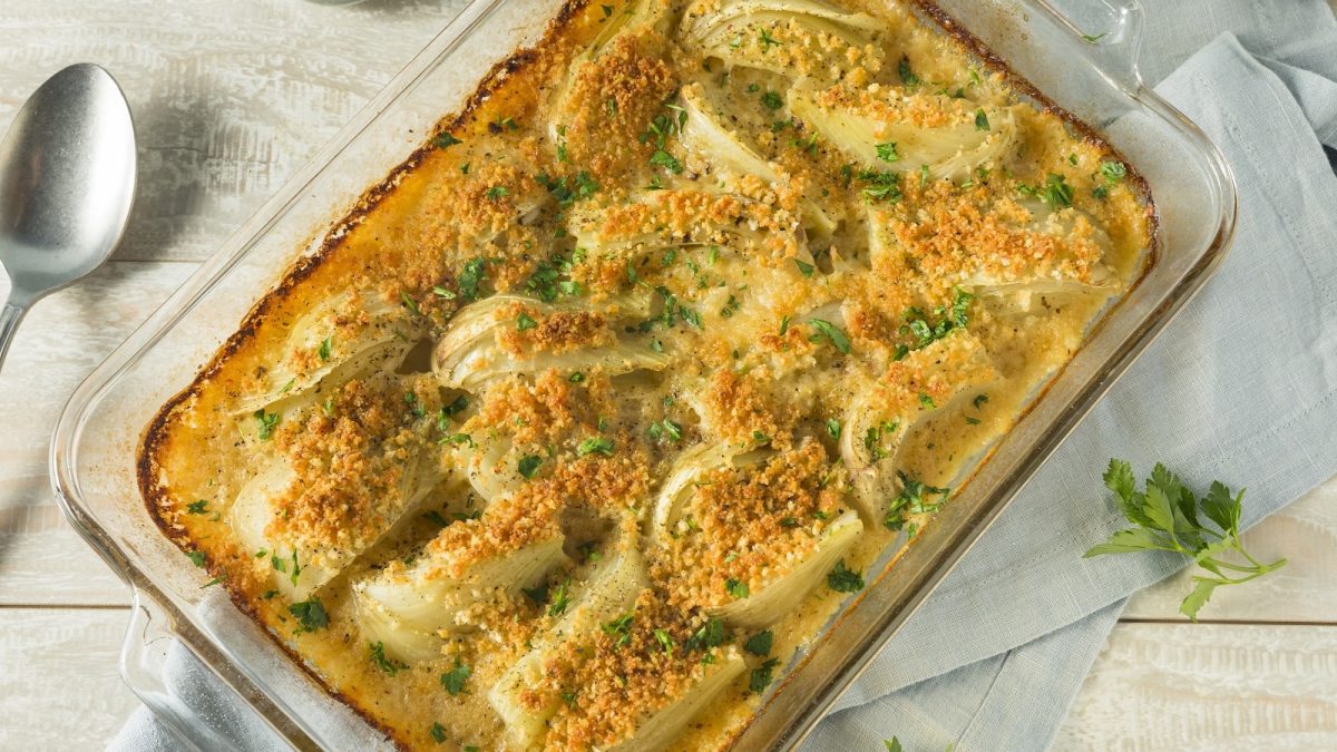 Eine gläserne Auflaufform mit Fenchel-Gratin auf einem hellgrauen Küchentuch.