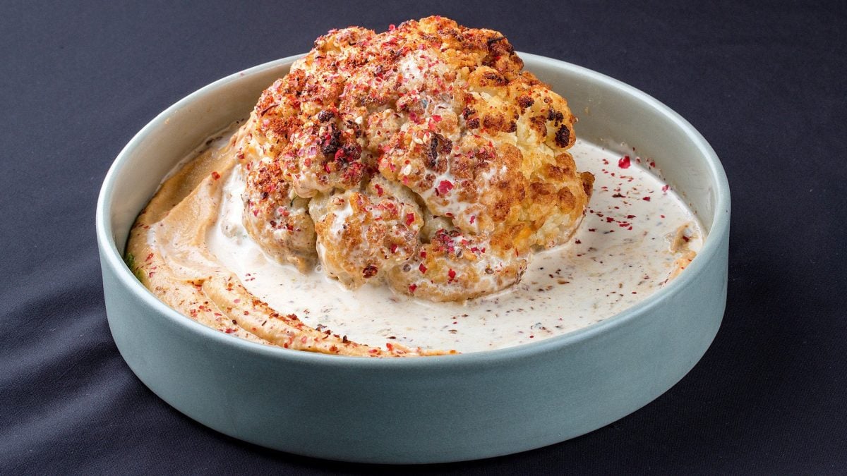 Eine hellblaue Schale mit gebackenem Blumenkohl auf Hummus.
