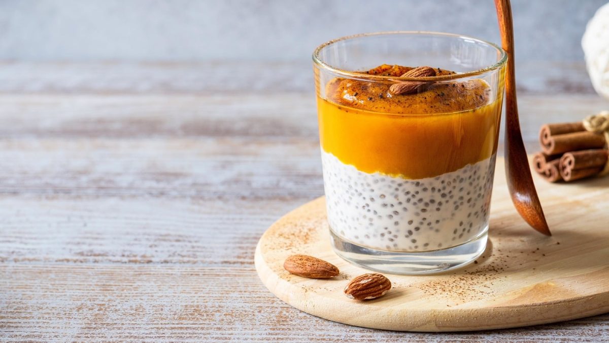 Ein Glas mit Kürbis-Chiapudding auf einem ovalen Holzbrett