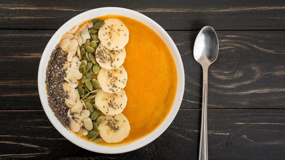 Eine Kürbis-Smoothie-Bowl auf einem dunklen Holztisch.