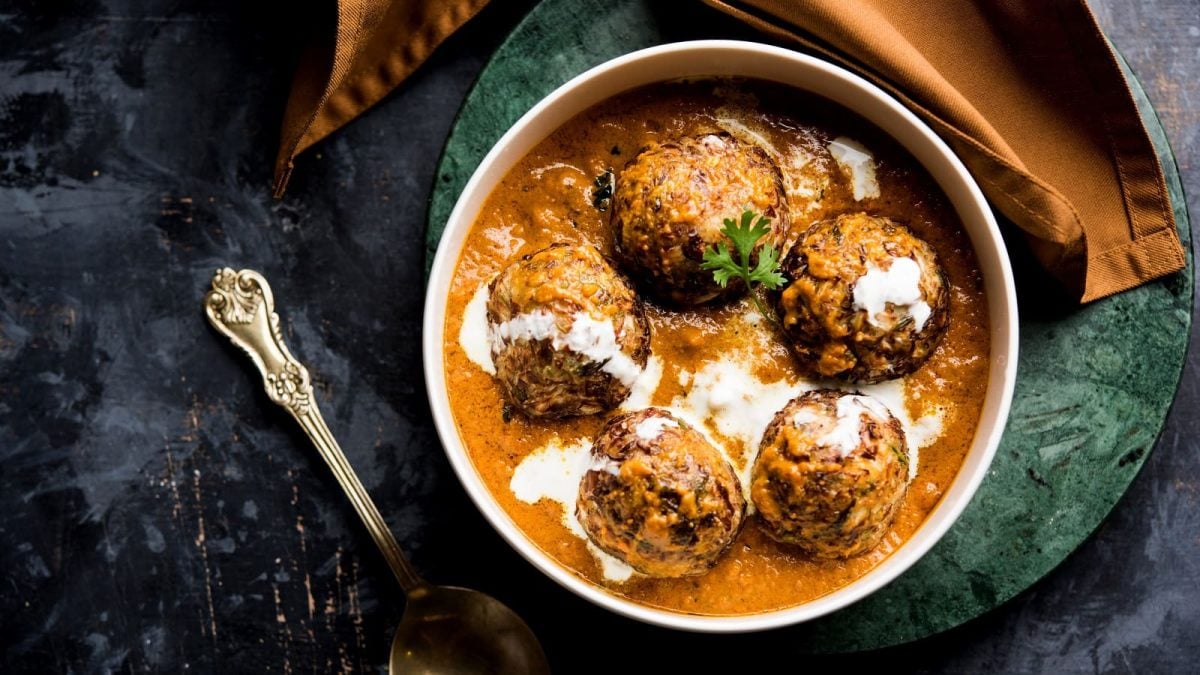 Eine weiße Schüssel mit Malai Kofta auf einem dunkelgrünen Tuch.