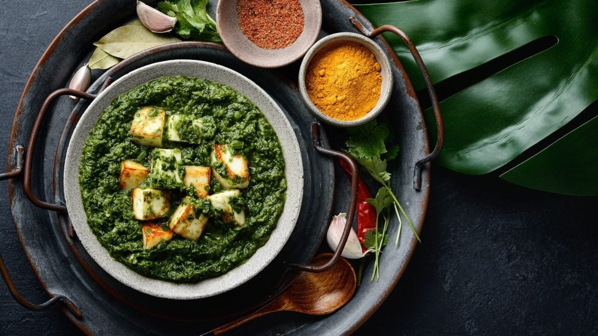 Eine Schüssel mit Paneer Palak darauf neben Gewürzen.
