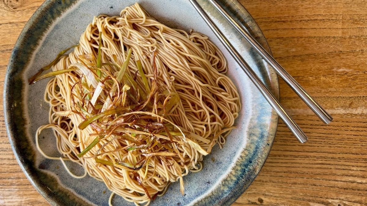 Ein Keramikteller mit Scallion Oil Noodles auf einem Holztisch.