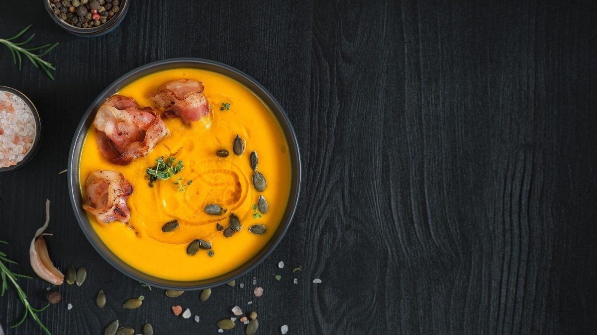 Eine schwarze Schüssel mit Speck-Kürbissuppe auf schwarzem Hintergrund.