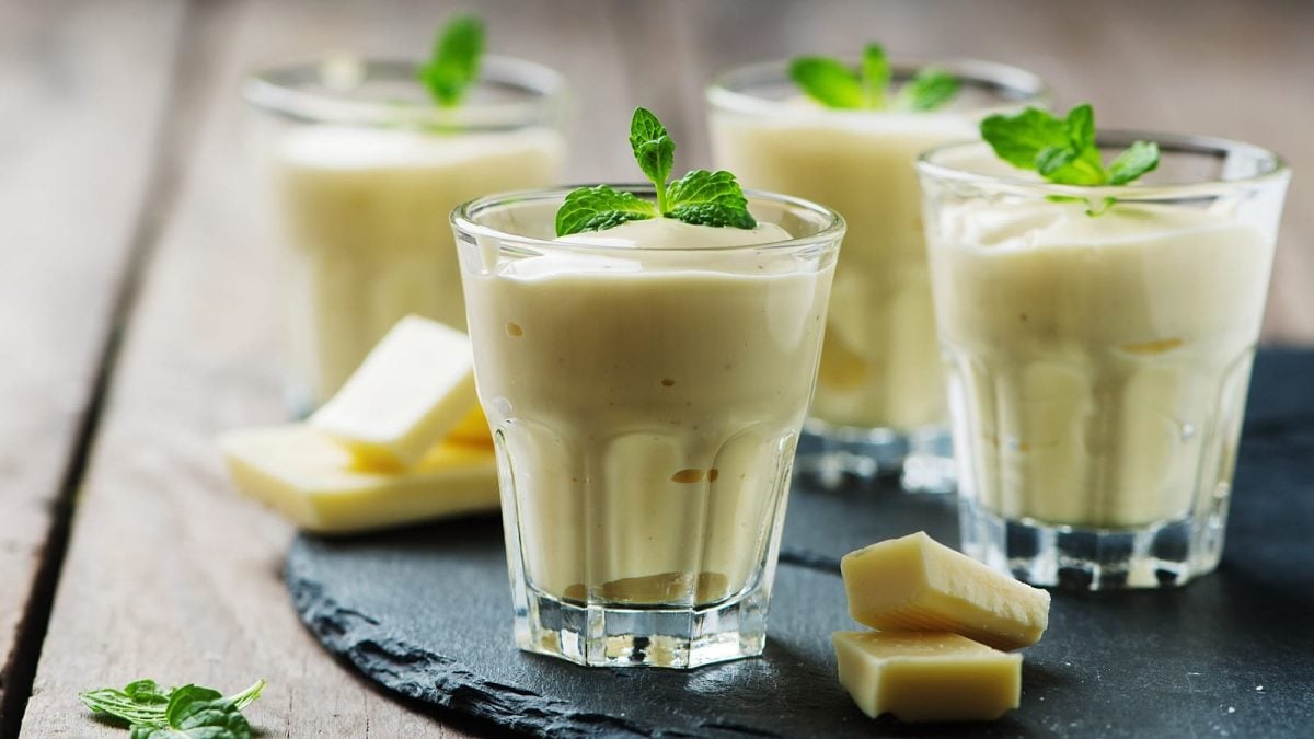 Vier Gläser mit Weiße-Schokoladen-Mousse auf einem Schiefer-Tablett.