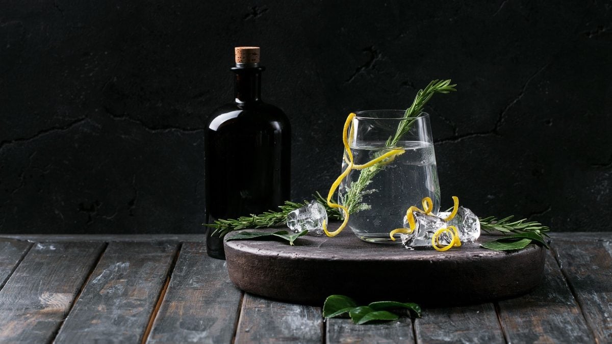 Ein Glas Gin Tonic Spritz mit Rosmarin und Orangenzeste, daneben eine dunkle Flasche Gin.