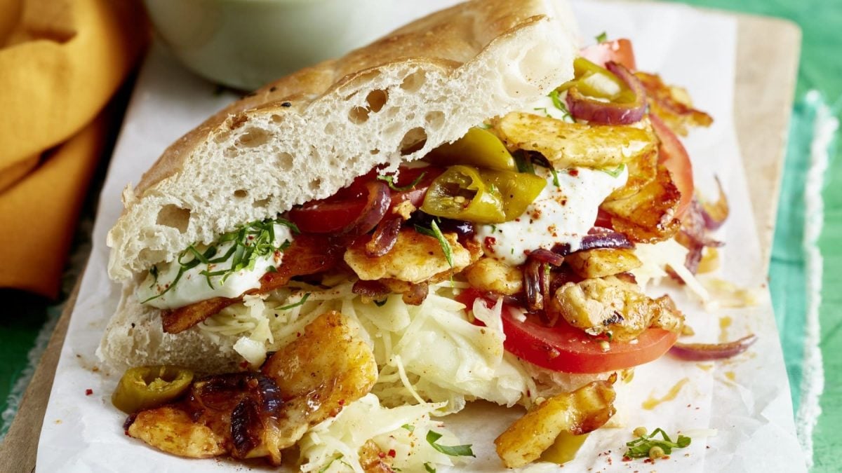 Vegetarisches Halloumi-Gyros im Fladenbrot auf weißem Papier und Holzbrett. Frontalansicht.