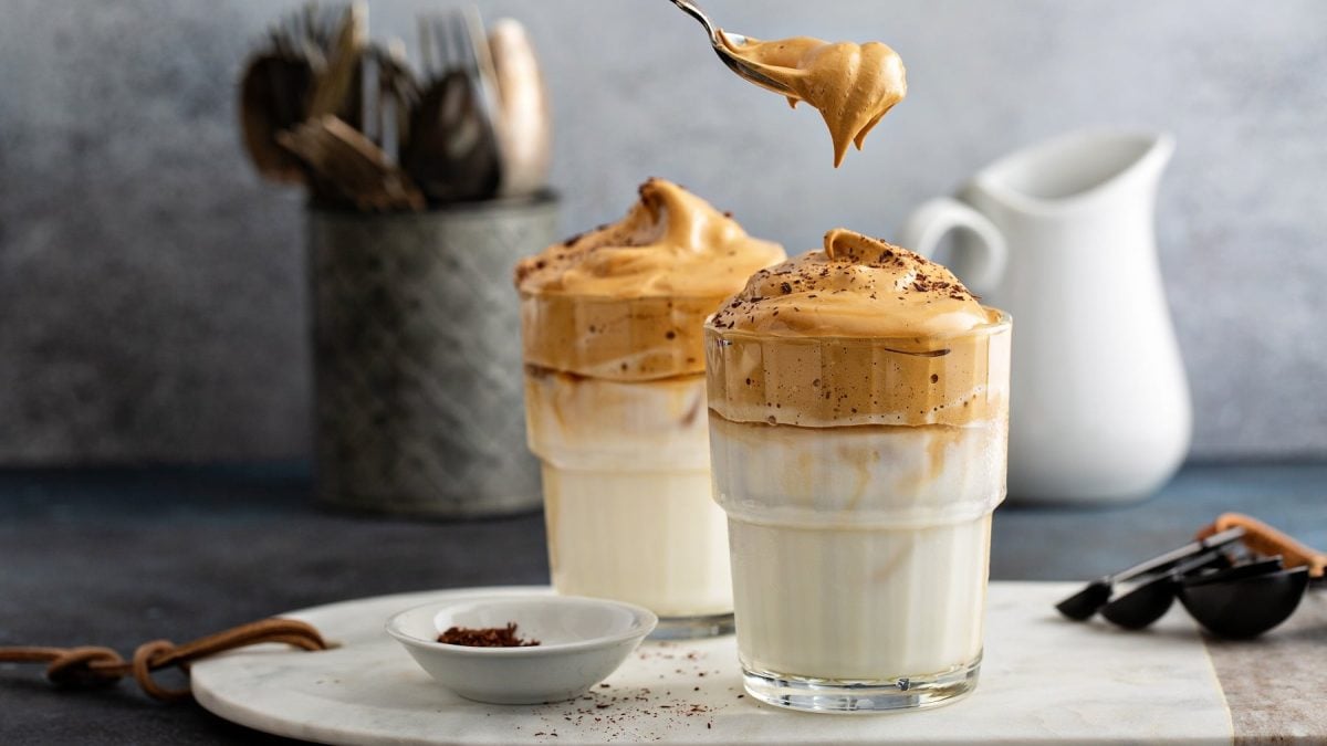 Zwei Gläser heißer Dalgona Coffee, außerdem ein Besteckkorb, ein Milchkännchen und eine Schale mit Gewürzen.
