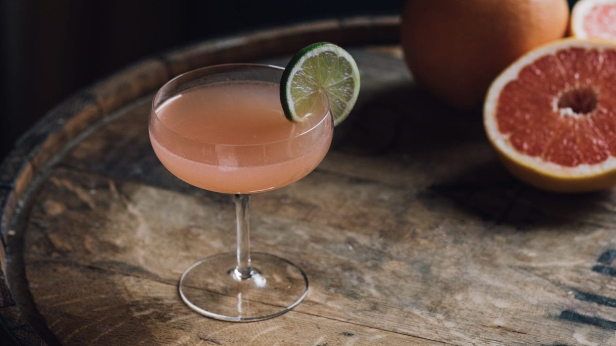 Hemingway Special Daiquiri Papa Doble mit Limettenscheibe auf Holzfass. Daneben Blutorange. Draufsicht.