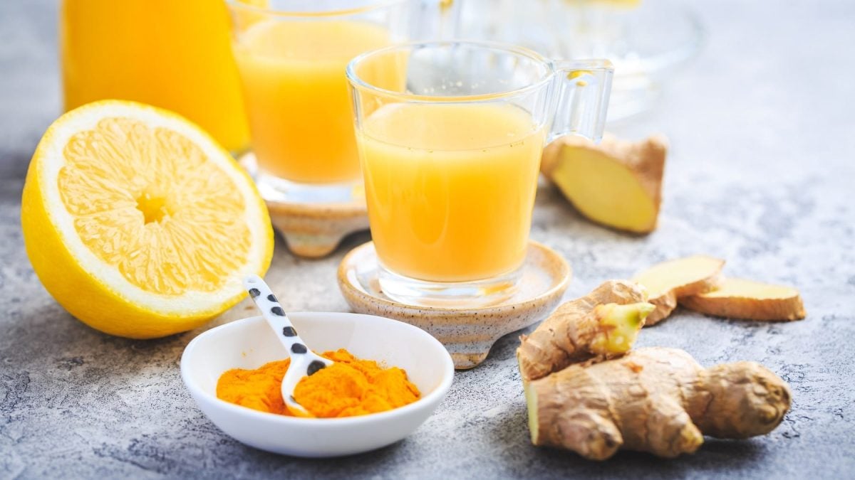 Zwei Gläser mit selbst gemachten Ingwer Shots, daneben lieben die Zutaten: Orangen, Ingwer ud Kurkumapulver.