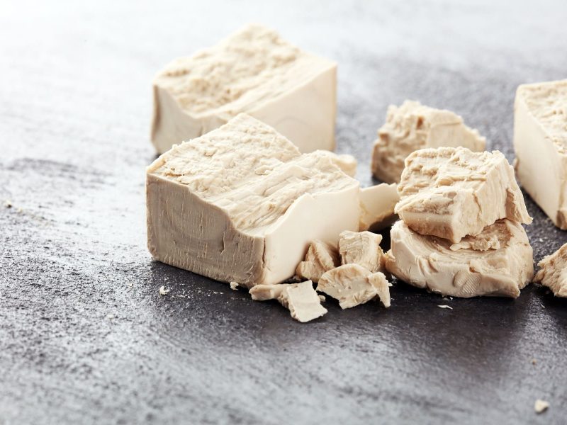Ist Hefe vegan: zerbröselte Hefewürfel auf grauem Untergrund.