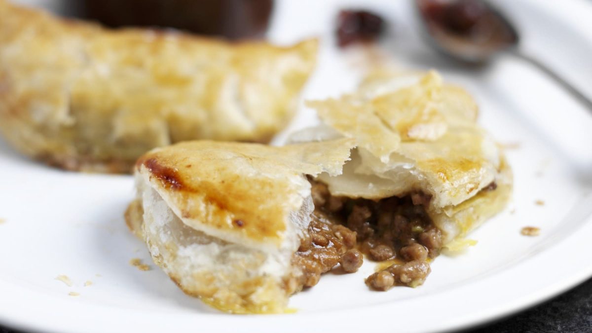 Tourtière-Pastete, bestehend aus Blätterteig und einer Hackfleischfüllung, aufgeschnitten serviert auf einem weißen Teller.