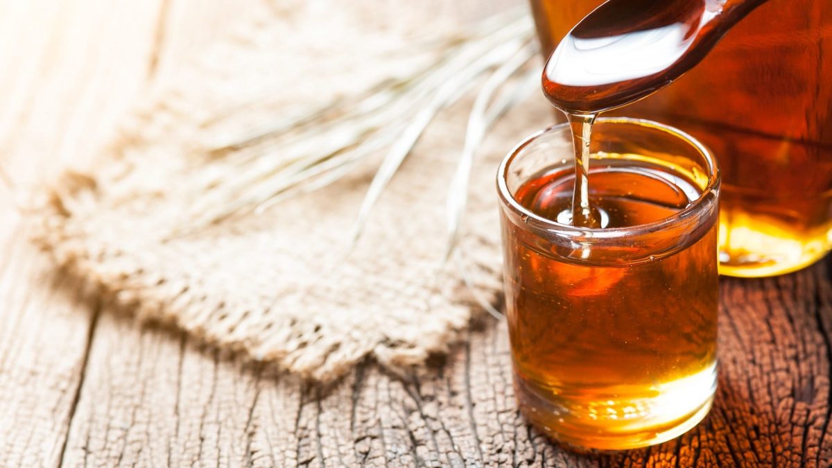 Ein kleines Glas Karamellsirup mit Zimt, über dem ein Holzlöffel gehalten wird.