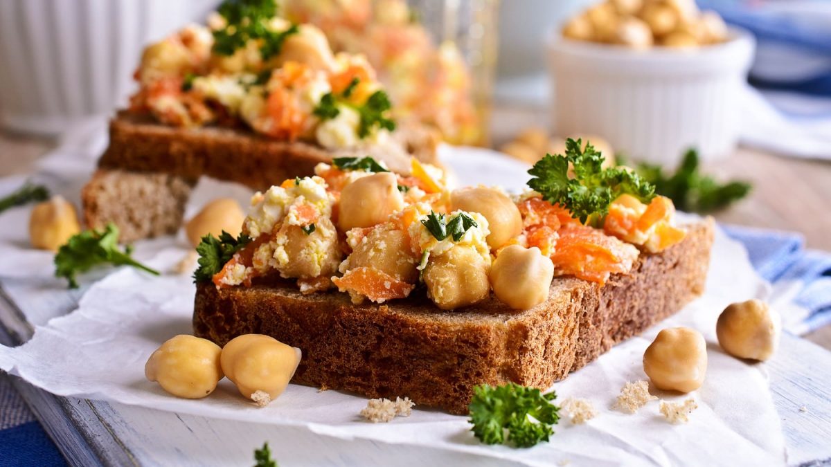 Zwei Kichererbsen-Karotten-Sandwiches auf Butterbrotpapier, im Hintergrund eine Schale Kichererbsen.