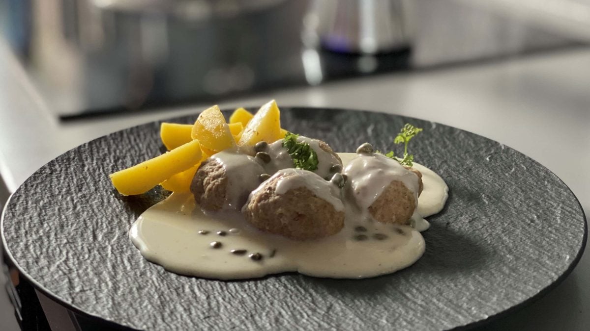 Original Königsberger Klopse mit Salzkartoffeln auf schwarzem Teller auf Küchenzeile. Frontalansicht.