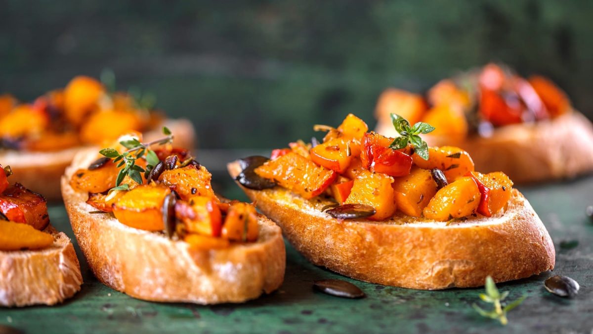 Mehrere Kürbis-Bruschetta mit Kürbiskernen und frischen Kräutern.