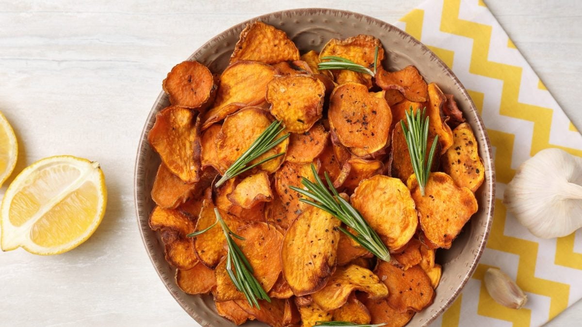 Eine Schale Kürbis-Chips mit Rosmarin in der Draufsicht, daneben Knoblauch und Zitronenspalten.