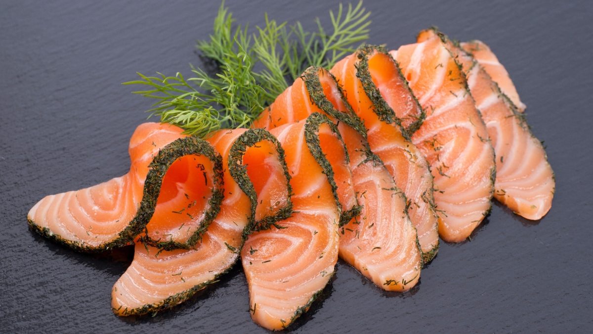 Gebeizter Lachs in Scheiben auf einer schwarzen Schieferplatte.