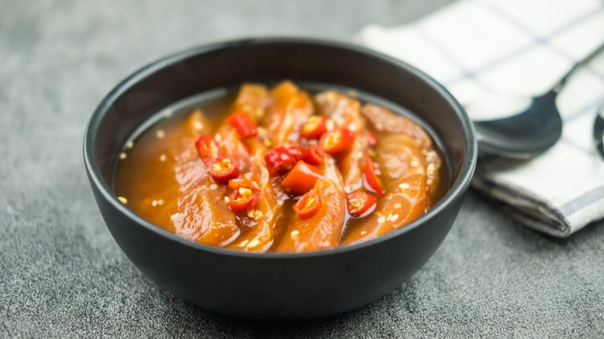 Eine schwarze Schale mit dem gebeizten Lachs auf einem grauen Untergrund. Im Hintergrund ein weißes Küchentuch.