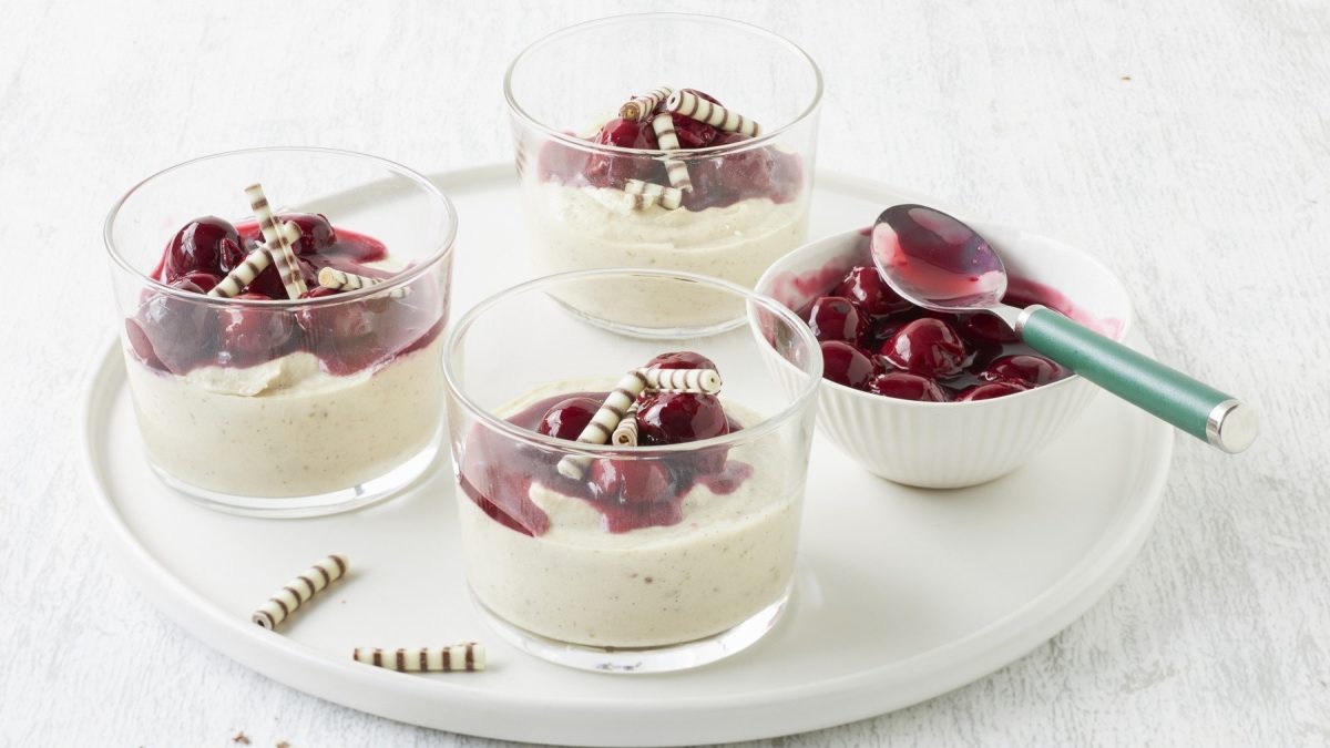 Maronenmousse mit Kirschen und Schokoröllchen in kleinen Gläsern vor weißem Hintergrund.