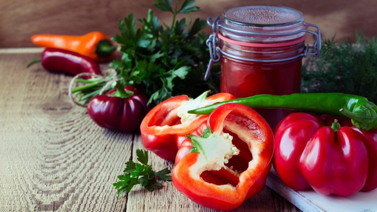 Selbst gemachte Paprikasauce in Weckglas auf Holz. Daneben Paprika und Gewürze. Frontalansicht.
