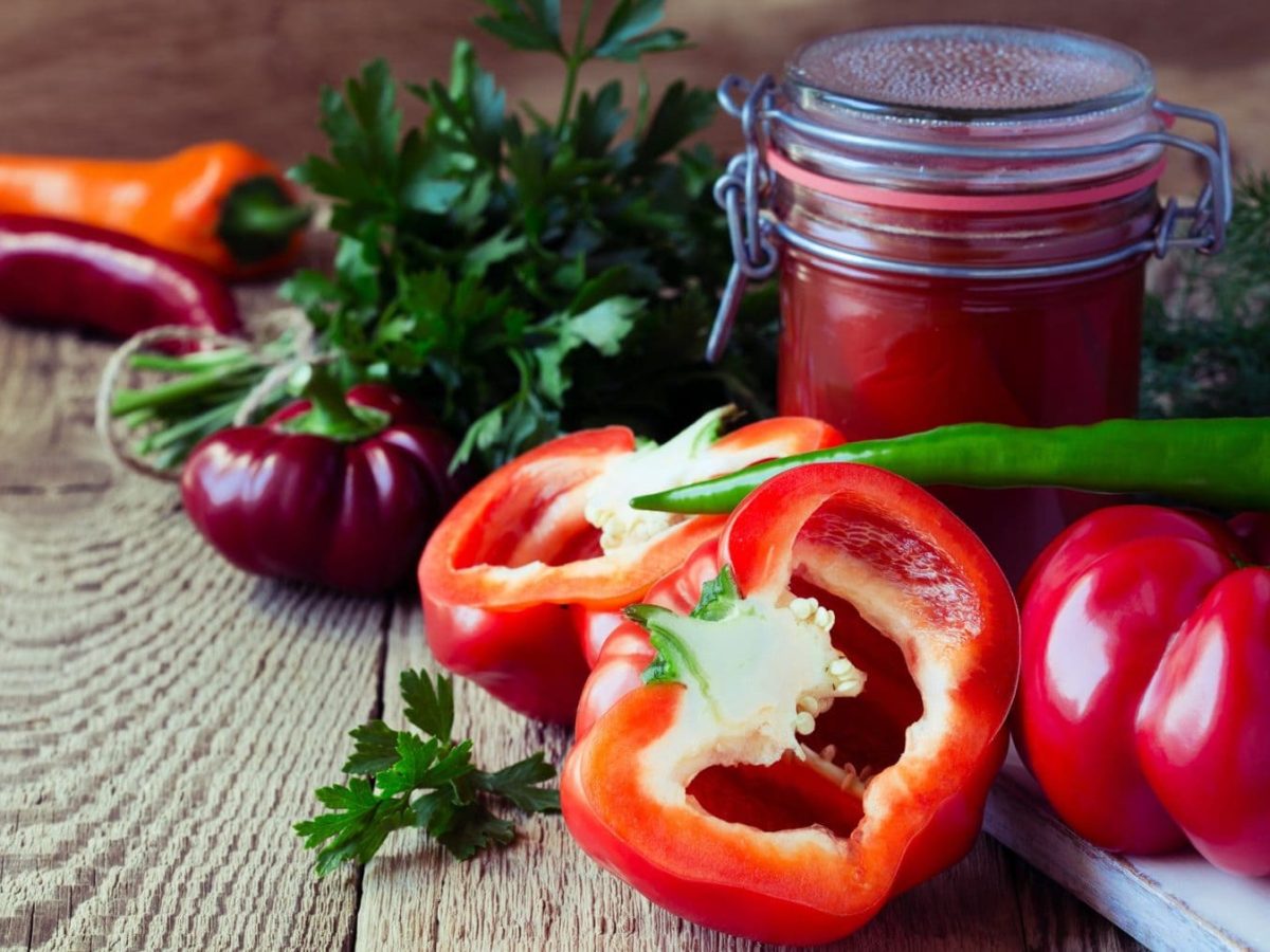 Selbst gemachte Paprikasauce in Weckglas auf Holz. Daneben Paprika und Gewürze. Frontalansicht.