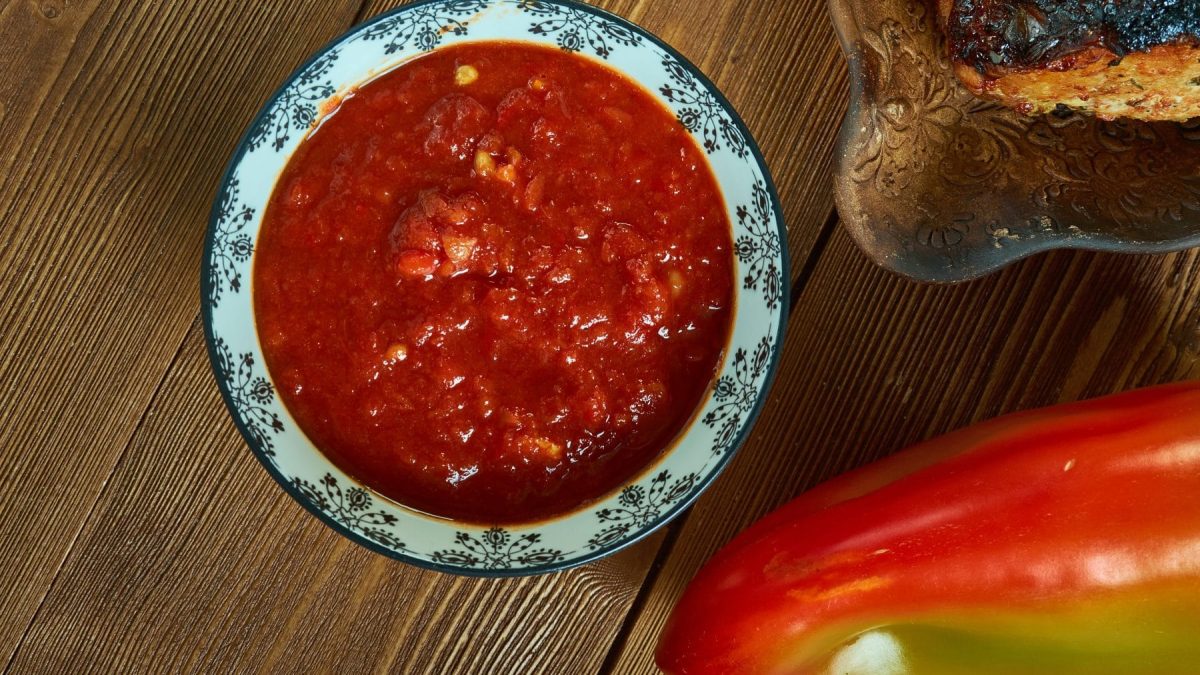 Salsa Ranchera in blau-weißer Schale auf Holztisch. Daneben Paprika und Toastbrot auf Teller. Draufsicht.