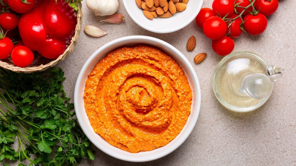 Salsa Romesco in weißer Schale, Petersilie, Tomaten, Mandeln und Essig auf einem Tisch. Draufsicht.