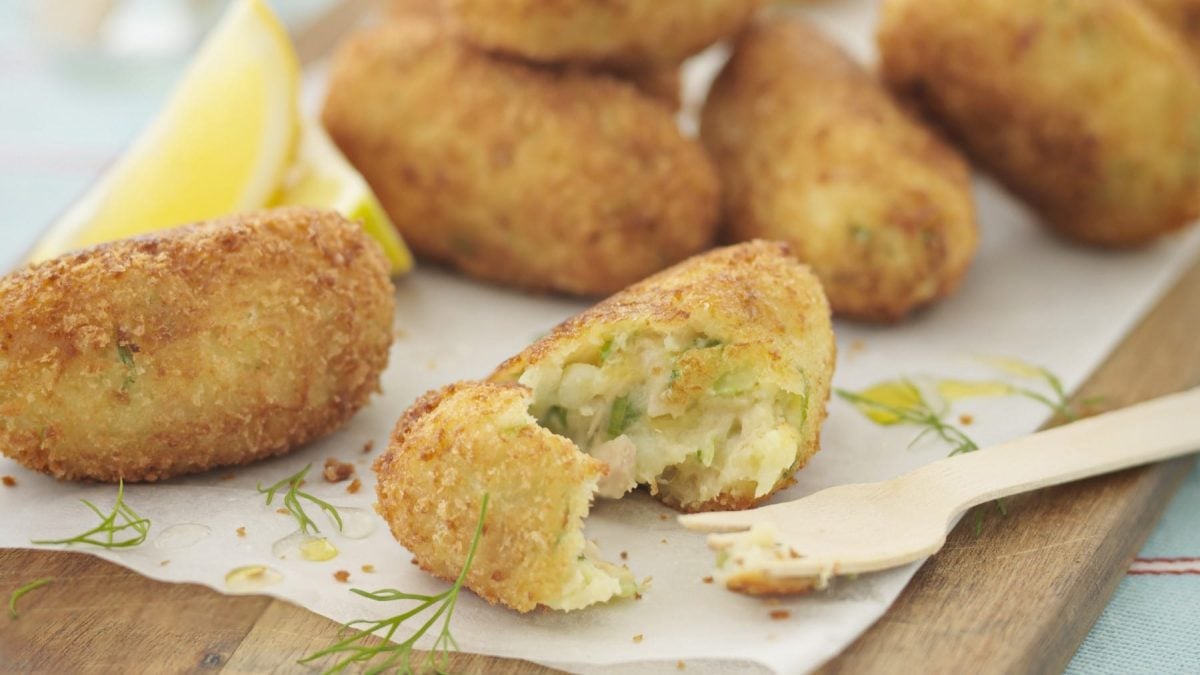 Selbst gemachte Thunfisch-Kroketten, angeschnitten serviert auf einem hellen Backpapier, garniert mit frischem Dill und serviert mit Zitronenstücken.