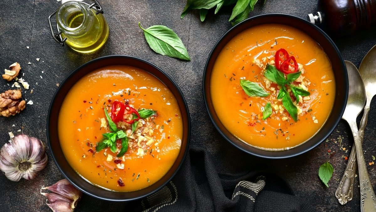 Zwei schwarze Schüsseln mit Spiced Hokkaido-Suppe neben frischen Zutaten auf einem dunklen Tisch.