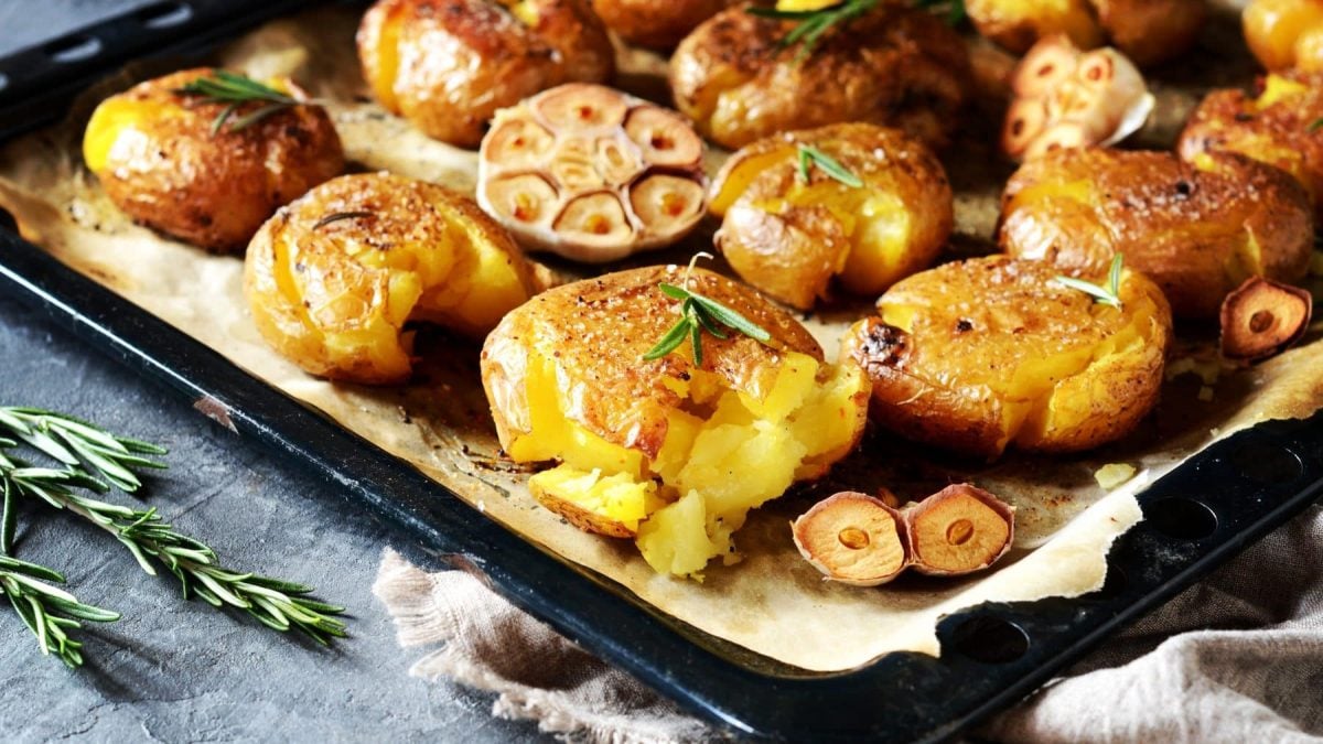 Smashed Garilc-Potatoes auf Backblech. Davor Rosmarinzweig. Draufsicht.