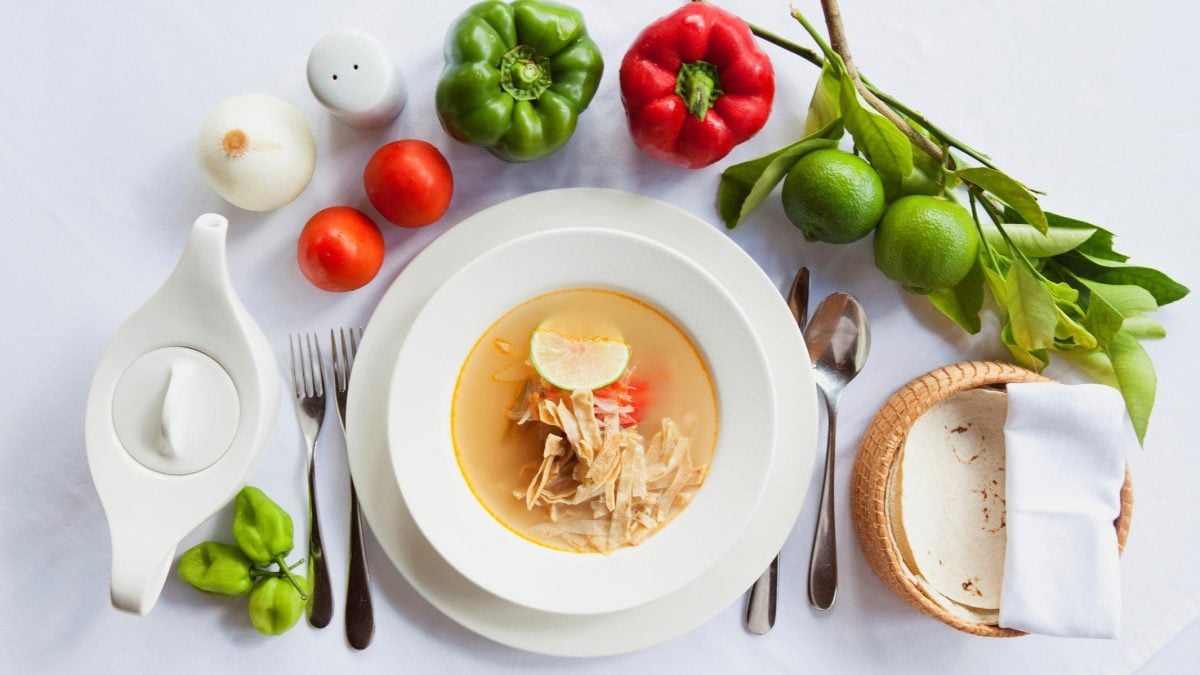 Sopa de Lima mexikanische Hühnersuppe auf Suppenteller auf Teller. Kreisförmig diverse Zutaten um den Teller herum angerichtet. Draufsicht.