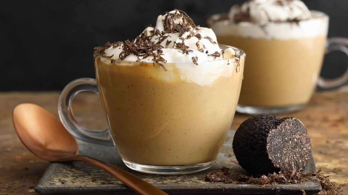 Zwei Glastassen Steinpilz-Cappuccino mit Trüffelsahne, daneben Löffel und Trüffel vor dunklem Hintergrund.