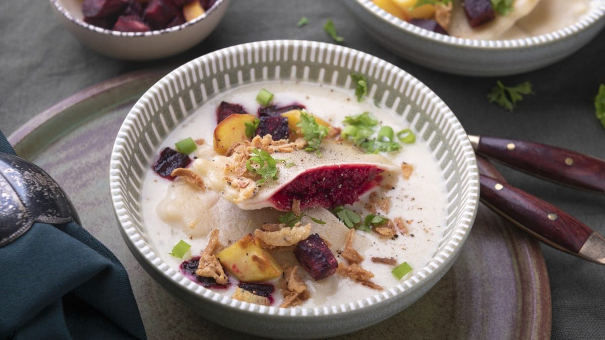 Vegane Maultaschen mit Rote-Bete-Füllung in heller Sauce in einer Schüssel vor dunklem Hintergrund.