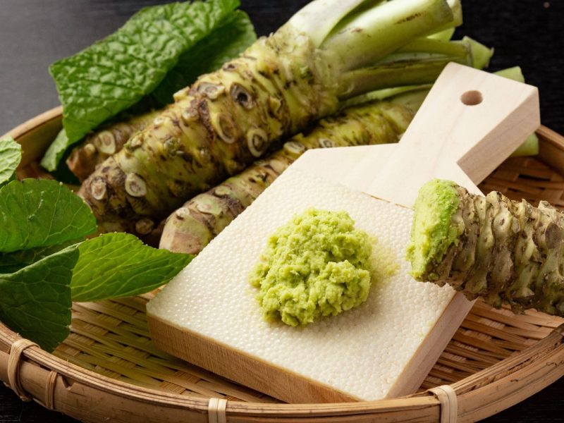 Eine Wasabi-Reibe in einem Holzkorb mit Wasabi-Stämmen.