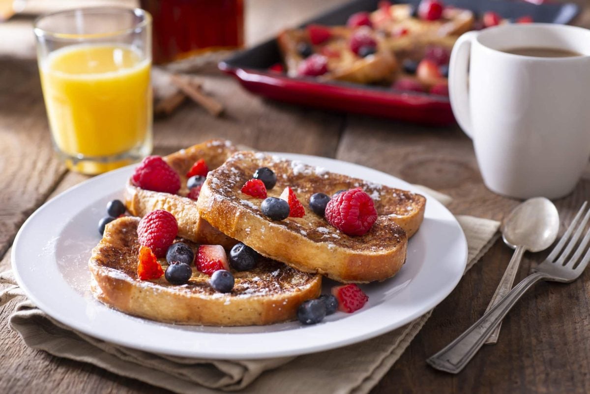 Arme Ritter mit Beeren und Puderzucker auf weißem Teller.