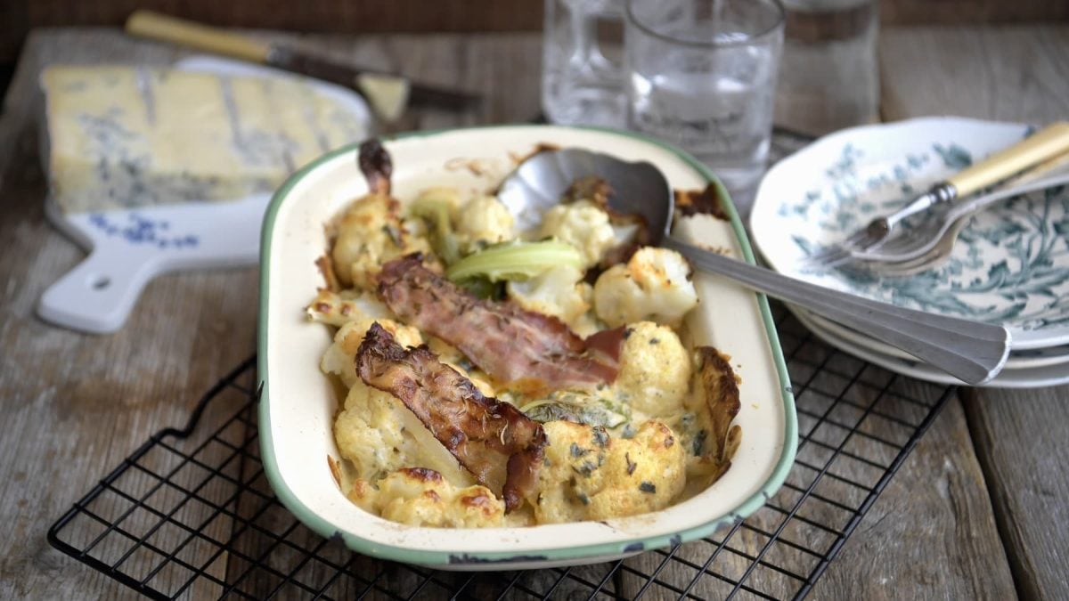 Blumenkohlgratin mit Blauschimmelkäse und geröstetem Speck, serviert in einer klassischen Auflaufform auf einem Gitter.