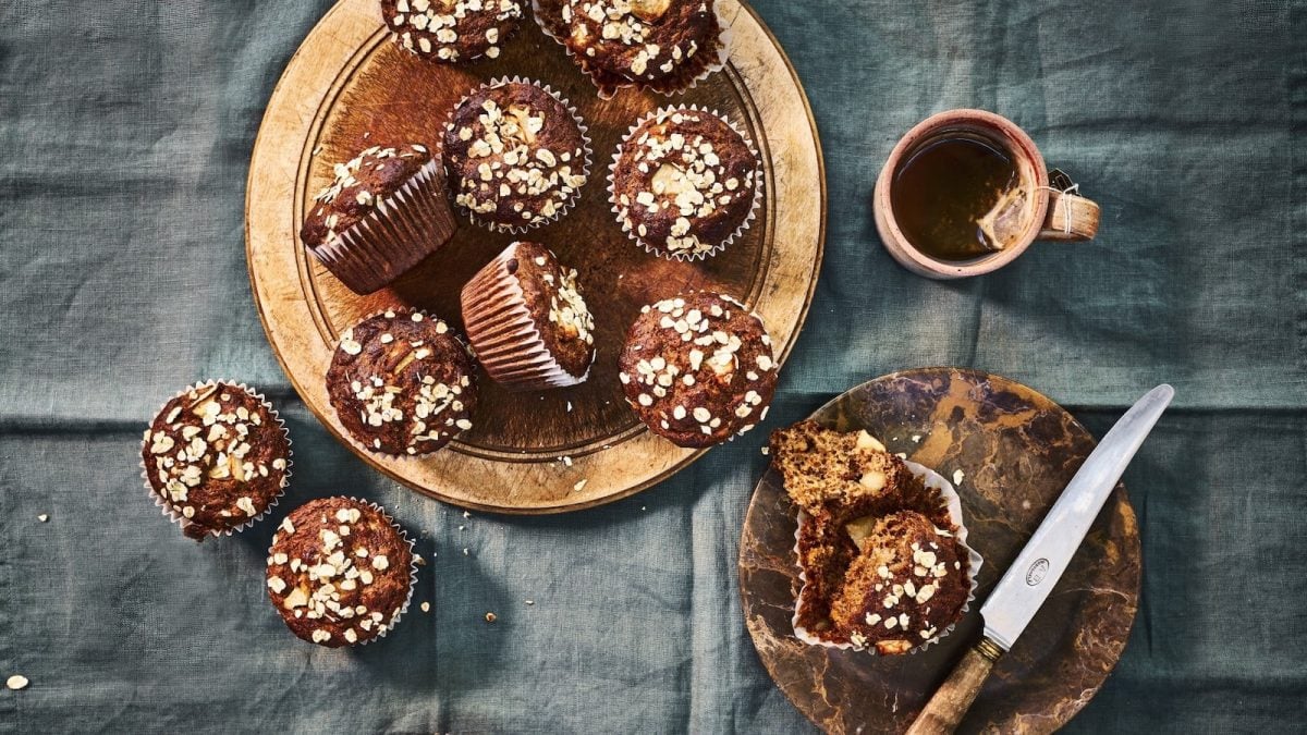 Apfelmuffins bestreut mit Haferflocken serviert auf einem braunen Holzteller und einer Tasse Tee