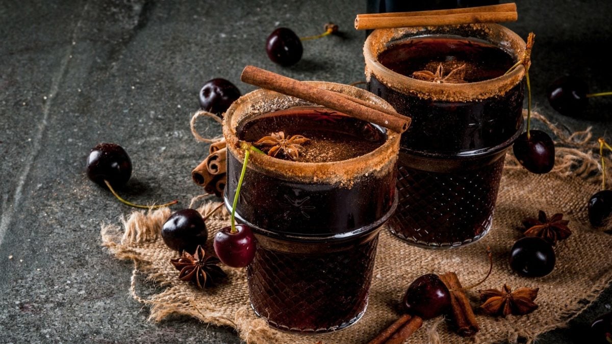 Zwei Gläser Glühwein mit Amaretto und Kirschen mit Zimtrand dekoriert mit Zimtstangen und Kirschen vor dunklem Hintergrund.