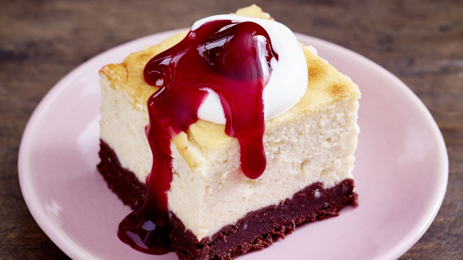 Ein Stück Käsekuchen mit Glühweinkirschen auf einem rosa Teller vor Holzhintergrund.