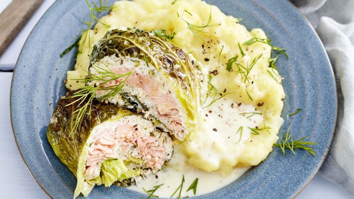 Lachs-Wirsing-Wickel mit Kartoffelbrei und Dill auf einem blauen Teller vor hellem Hintergrund.