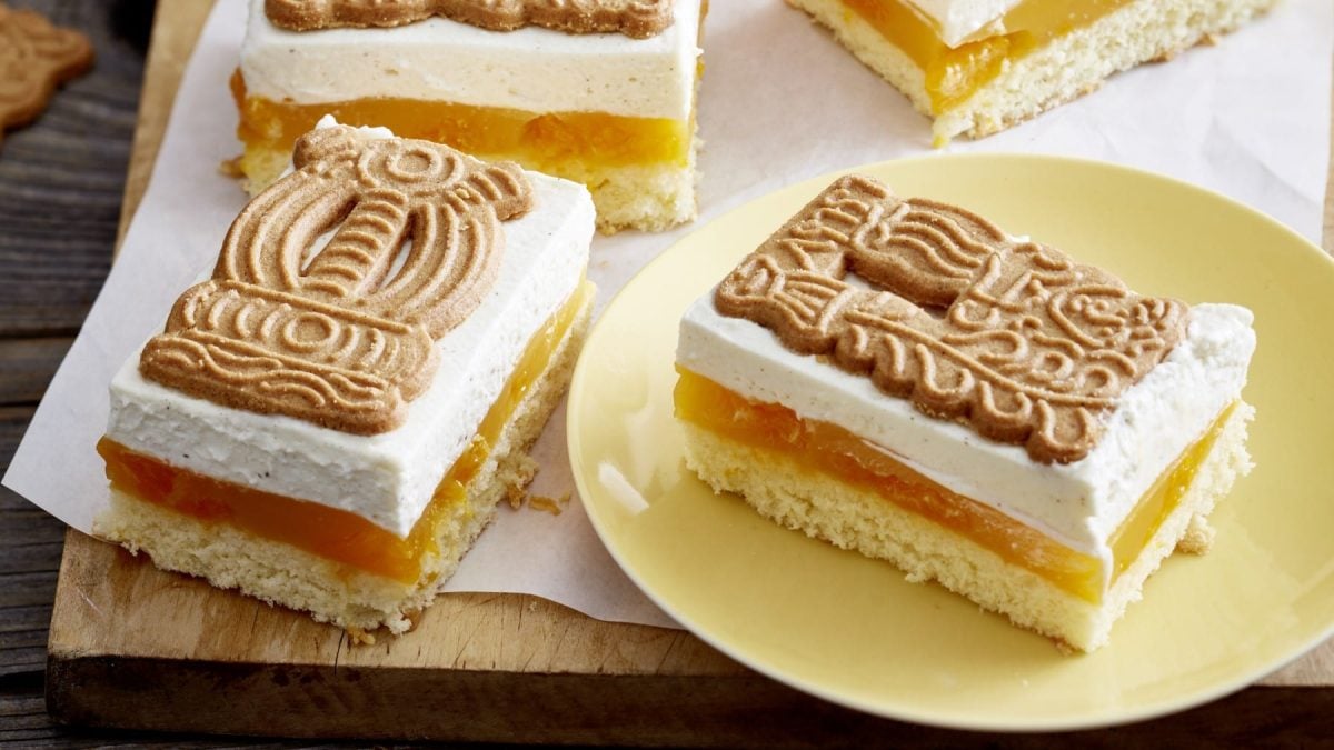 Auf einem Teller liegen zwei Stück Mandarinen-Spekulatius-Schnitten. Sie haben 2 Creme Schichten und einen Keks oben drauf.
