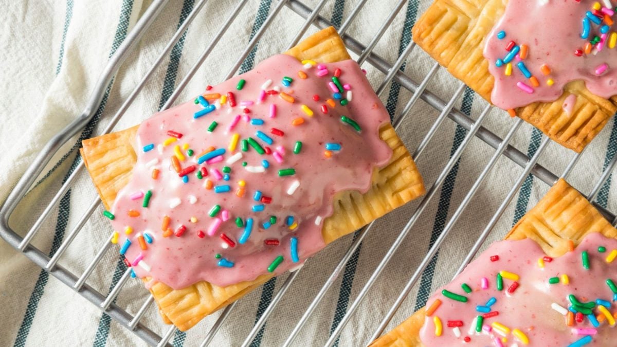 Selbst gemachte Pop Tarts mit rosa Guss und bunten Streuseln auf einem Gitter mit Küchentuch im Hintergrund.