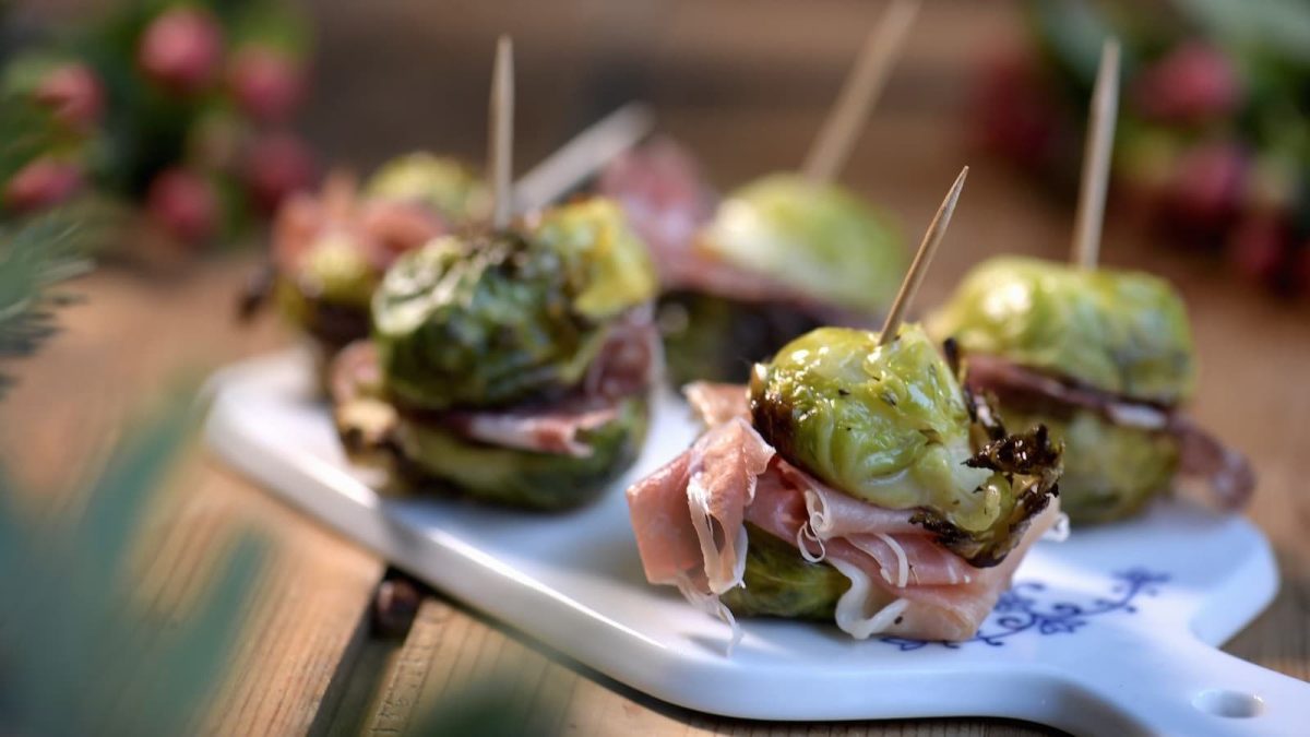 Halbierter Rosenkohl mit Salami und Parmaschinken, fixiert mit einem Zahnstocher auf einem weißen Brett serviert