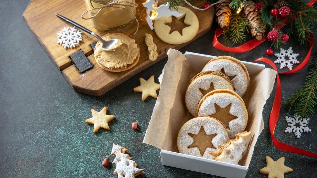 In einer Dose sind Linzer Plätzchen mit Erdnussbutter gelegt. Sie sind mit Puderzucker bestreut.