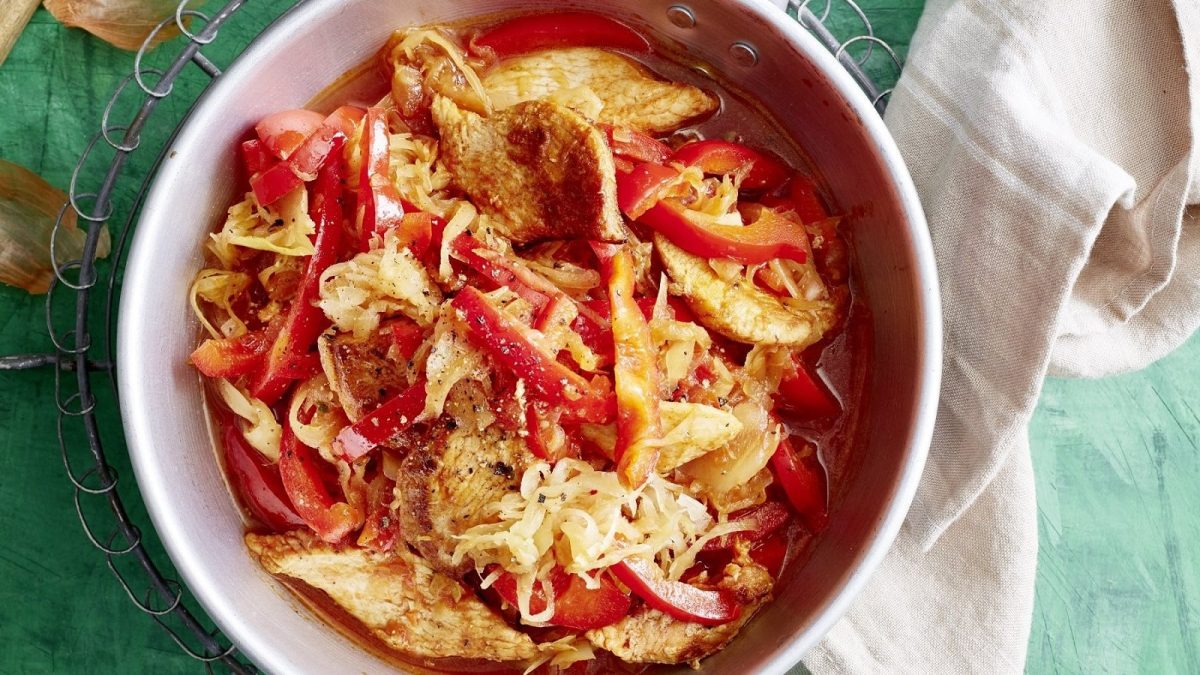 In einer Schüssel ist eine Sauerkraut-Puten-Pfanne angerichtet. Sie ist mit roter Paprika verfeinert.
