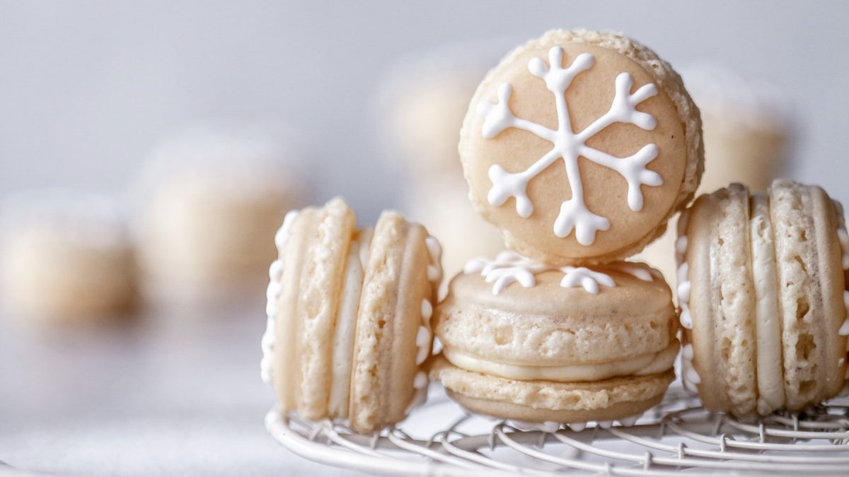 Einige Schneeflocken-Macarons auf einem Gitter platziert vor hellem Hintergrund mit weiteren Macarons verschwommen im Hintergrund.